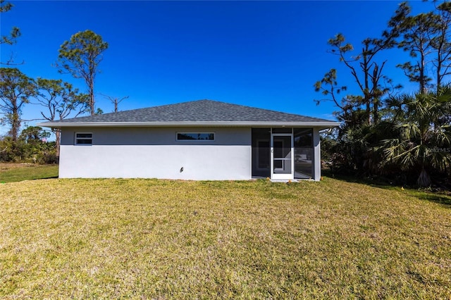 rear view of property featuring a yard, roof with shingles, a sunroom, and stucco siding