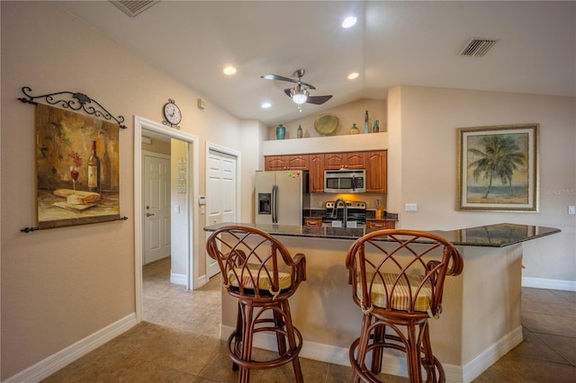 kitchen with visible vents, appliances with stainless steel finishes, brown cabinetry, a ceiling fan, and a kitchen breakfast bar