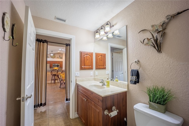 half bathroom featuring visible vents, a textured wall, toilet, tile patterned floors, and vanity