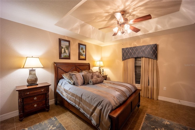 tiled bedroom featuring a ceiling fan, a tray ceiling, and baseboards