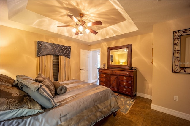 bedroom with ceiling fan, dark tile patterned flooring, a raised ceiling, and baseboards