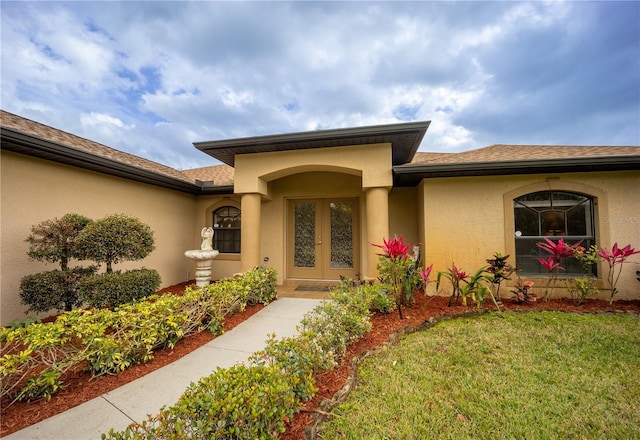 doorway to property featuring a shingled roof, a lawn, french doors, and stucco siding