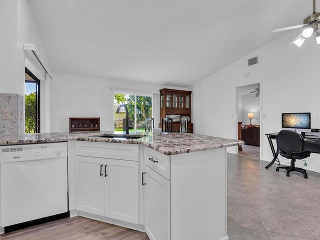 kitchen with lofted ceiling, light stone counters, white dishwasher, white cabinetry, and a sink