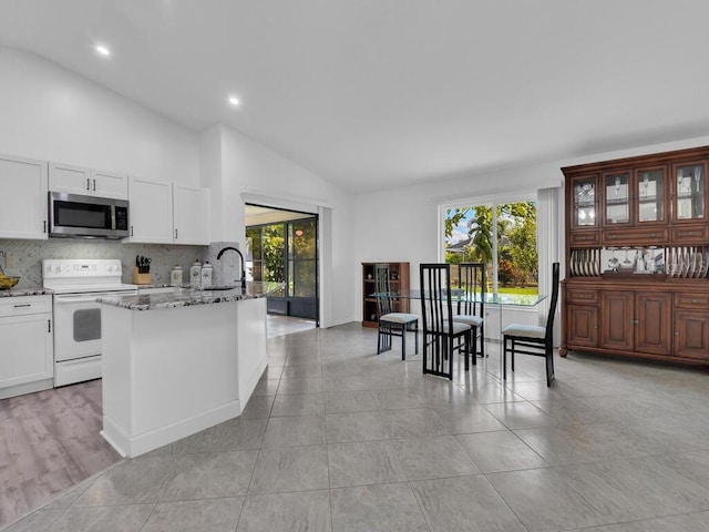 kitchen with stone countertops, stainless steel microwave, white cabinets, tasteful backsplash, and white range with electric cooktop