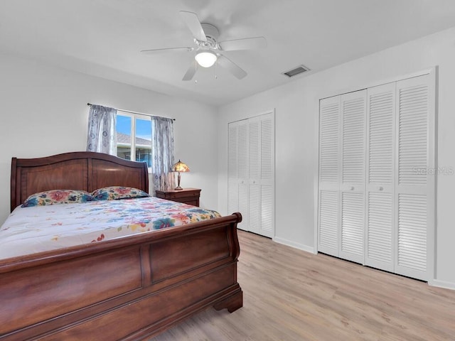 bedroom featuring baseboards, visible vents, ceiling fan, light wood-type flooring, and two closets