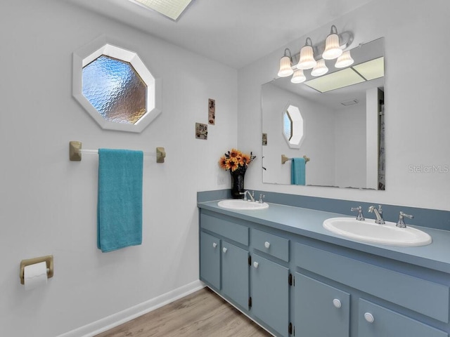 bathroom featuring double vanity, baseboards, a sink, and wood finished floors