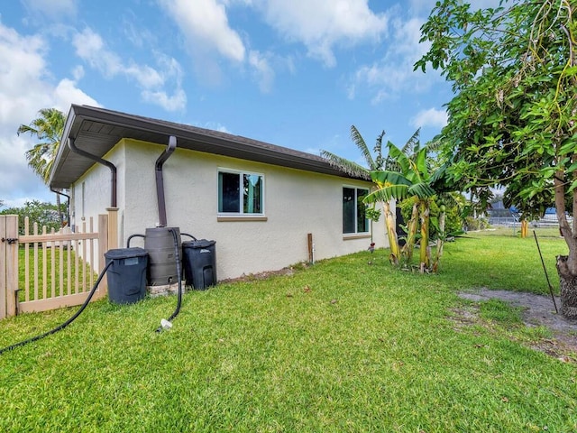 view of side of property with fence, a lawn, and stucco siding