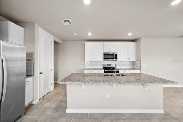 kitchen with stainless steel appliances, visible vents, backsplash, light stone countertops, and a kitchen bar