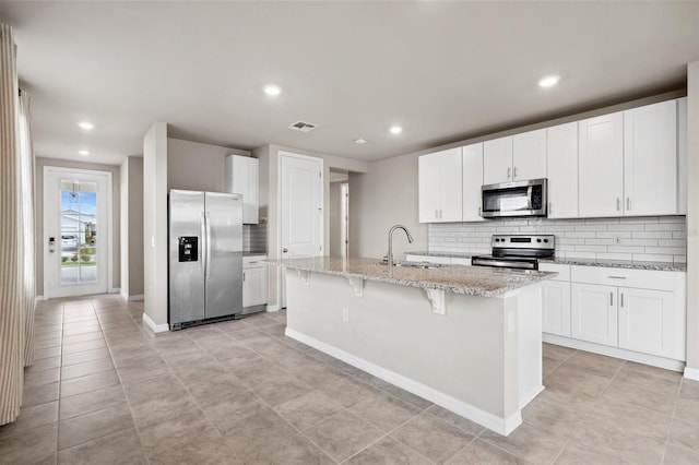 kitchen featuring light stone counters, stainless steel appliances, a sink, visible vents, and an island with sink