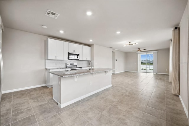 kitchen with a center island with sink, visible vents, light stone counters, stainless steel appliances, and backsplash