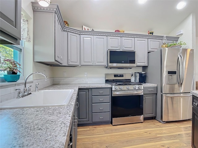 kitchen with light wood-style floors, stainless steel appliances, a sink, and gray cabinetry