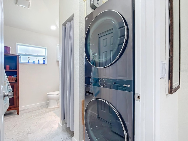 bathroom featuring toilet, stacked washing maching and dryer, baseboards, and marble finish floor