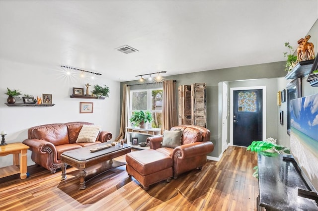 living area with baseboards, track lighting, visible vents, and wood finished floors