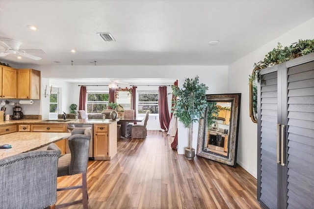 kitchen featuring visible vents, light wood-style flooring, a ceiling fan, a sink, and a peninsula