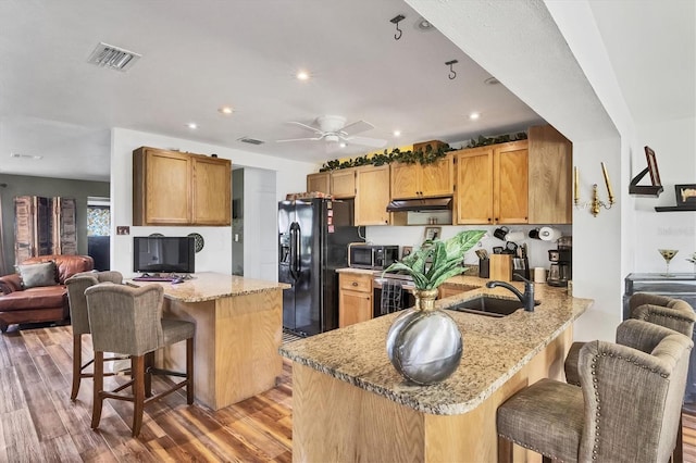 kitchen with visible vents, a peninsula, black fridge, under cabinet range hood, and a sink