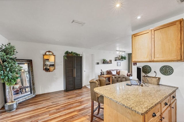 kitchen with light brown cabinets, light wood-style flooring, a breakfast bar, open floor plan, and light stone countertops