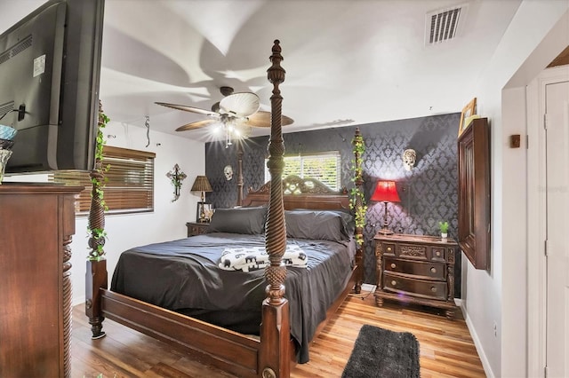 bedroom featuring an accent wall, wood finished floors, visible vents, and baseboards