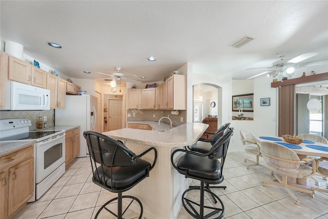 kitchen featuring a breakfast bar, white appliances, a ceiling fan, and light brown cabinets