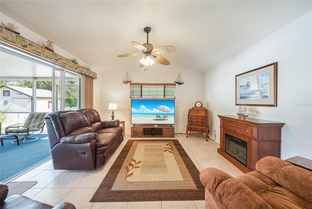 living area featuring light tile patterned floors, a glass covered fireplace, lofted ceiling, and a ceiling fan