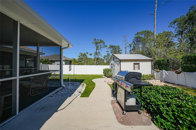 view of patio with an outbuilding, a storage unit, a fenced backyard, and a sunroom