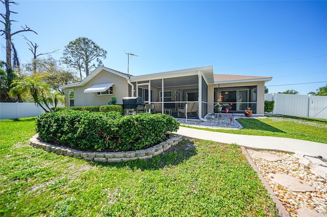 rear view of house featuring a yard, a fenced backyard, a sunroom, and stucco siding