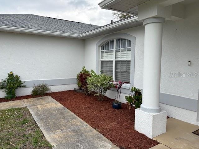 doorway to property featuring roof with shingles and stucco siding