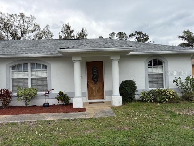 property entrance featuring a yard, a shingled roof, and stucco siding