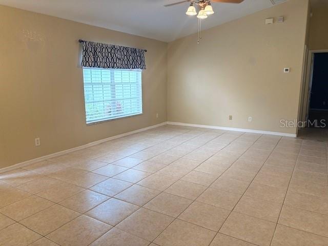 empty room with ceiling fan, baseboards, vaulted ceiling, and light tile patterned flooring