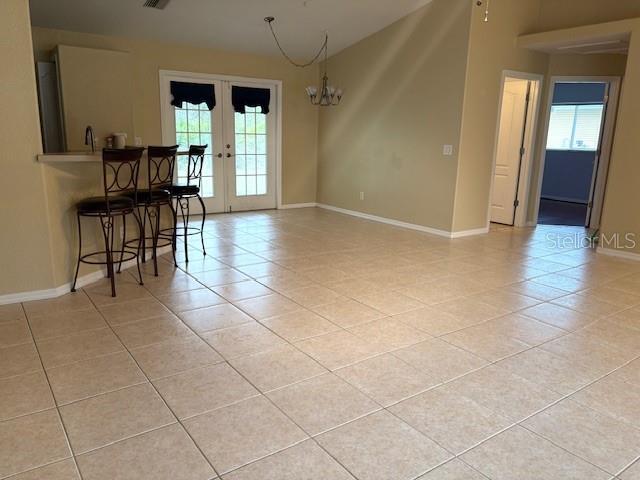 unfurnished dining area featuring french doors, plenty of natural light, light tile patterned flooring, and baseboards