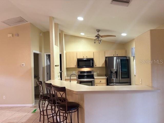 kitchen featuring light tile patterned floors, stainless steel appliances, light brown cabinets, vaulted ceiling, and a peninsula