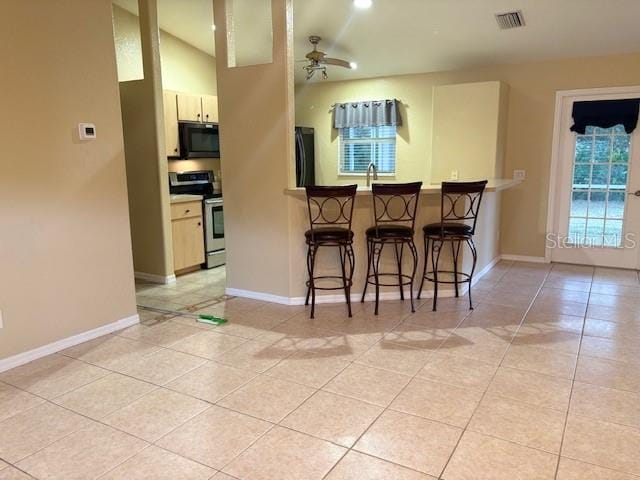 kitchen featuring ceiling fan, light tile patterned floors, a breakfast bar, visible vents, and black appliances