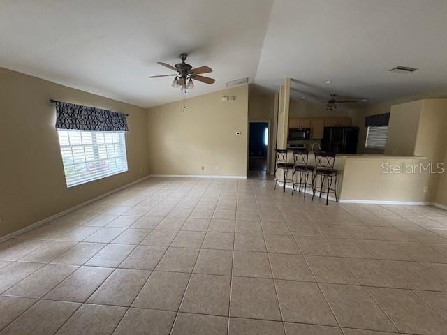 unfurnished living room with light tile patterned floors, ceiling fan, baseboards, and vaulted ceiling