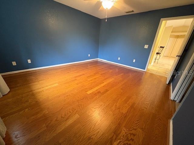 empty room featuring baseboards, visible vents, a ceiling fan, and wood finished floors