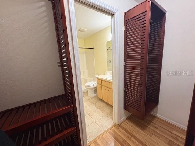 bathroom featuring toilet, vanity, wood finished floors, baseboards, and walk in shower