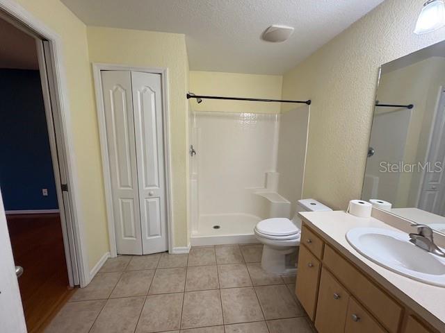 bathroom with toilet, tile patterned flooring, a shower, and a closet