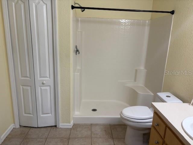 full bath featuring tile patterned flooring, toilet, vanity, baseboards, and a shower stall