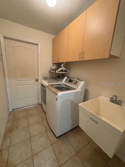 laundry room with a textured ceiling, light tile patterned flooring, a sink, cabinet space, and washing machine and clothes dryer