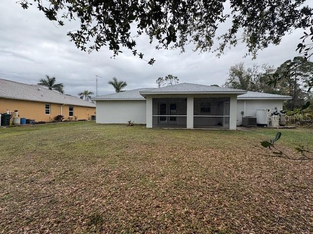 rear view of house with a sunroom, stucco siding, a yard, and central AC unit