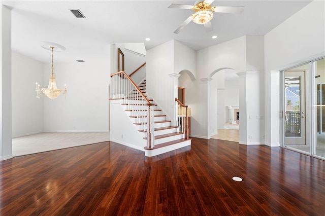 interior space featuring visible vents, a fireplace with raised hearth, stairway, wood finished floors, and ceiling fan with notable chandelier