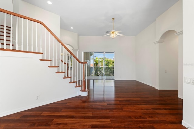 interior space with ceiling fan, arched walkways, wood finished floors, baseboards, and stairway