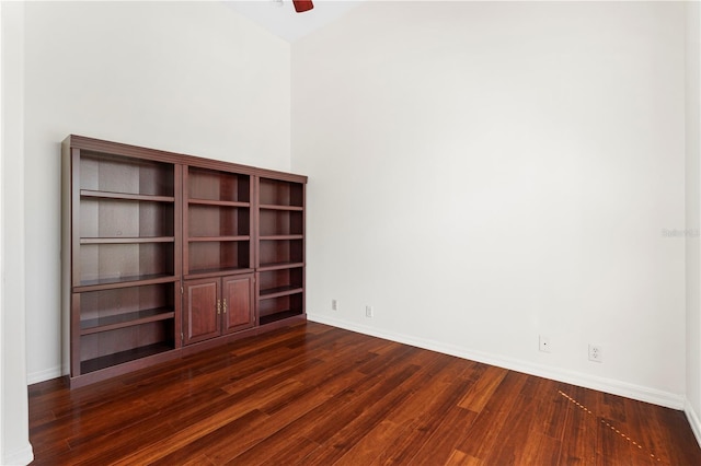 spare room with dark wood-type flooring, a ceiling fan, and baseboards