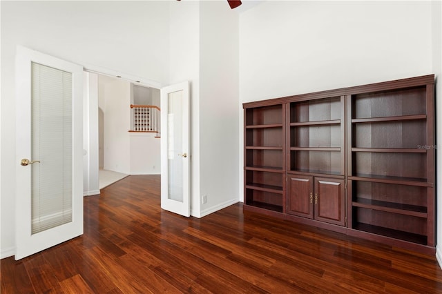 empty room with a towering ceiling, a ceiling fan, baseboards, and dark wood-type flooring