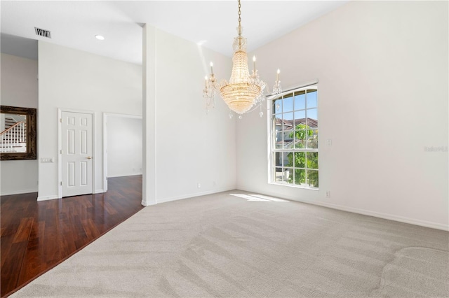 empty room with carpet floors, a high ceiling, visible vents, baseboards, and an inviting chandelier