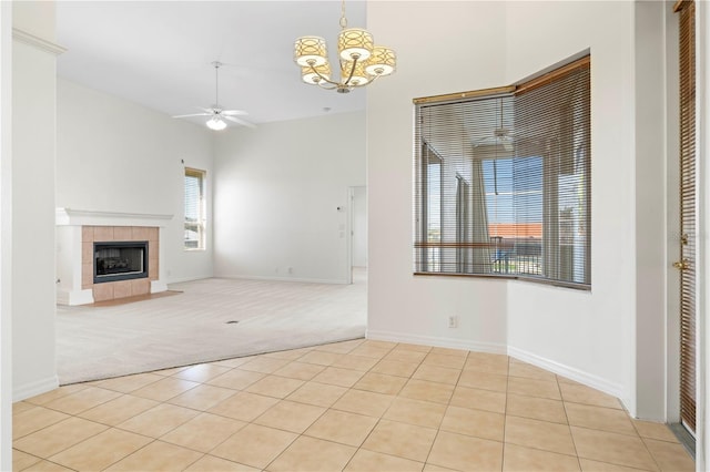 unfurnished living room featuring light tile patterned floors, a tile fireplace, light colored carpet, ceiling fan with notable chandelier, and baseboards