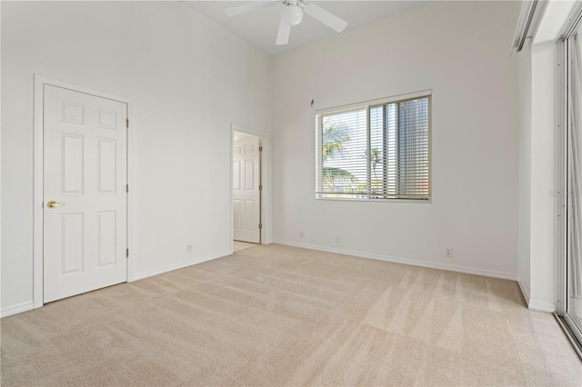 unfurnished bedroom featuring a high ceiling, baseboards, and light colored carpet