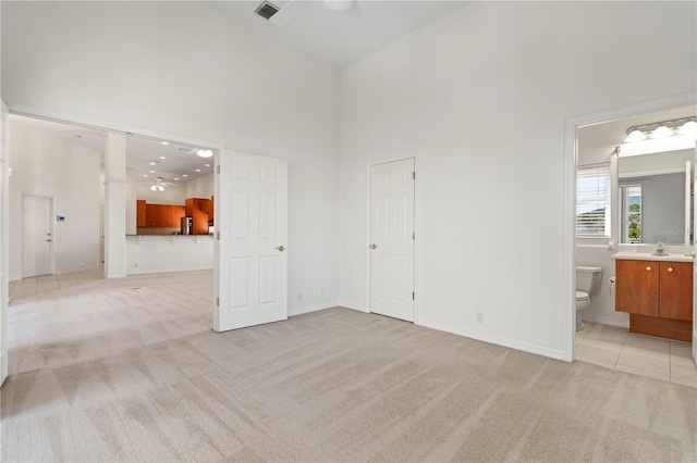 unfurnished living room featuring light tile patterned floors, light colored carpet, a high ceiling, visible vents, and baseboards