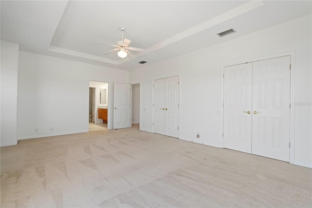 unfurnished bedroom with light carpet, a tray ceiling, visible vents, and multiple closets