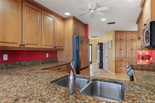 kitchen featuring visible vents, brown cabinetry, stainless steel microwave, freestanding refrigerator, and stone counters