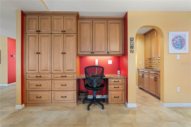 home office with arched walkways, light tile patterned flooring, and baseboards