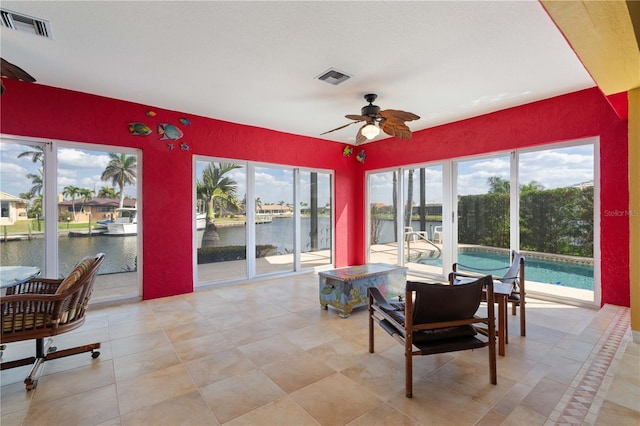 sunroom featuring ceiling fan, a water view, and visible vents